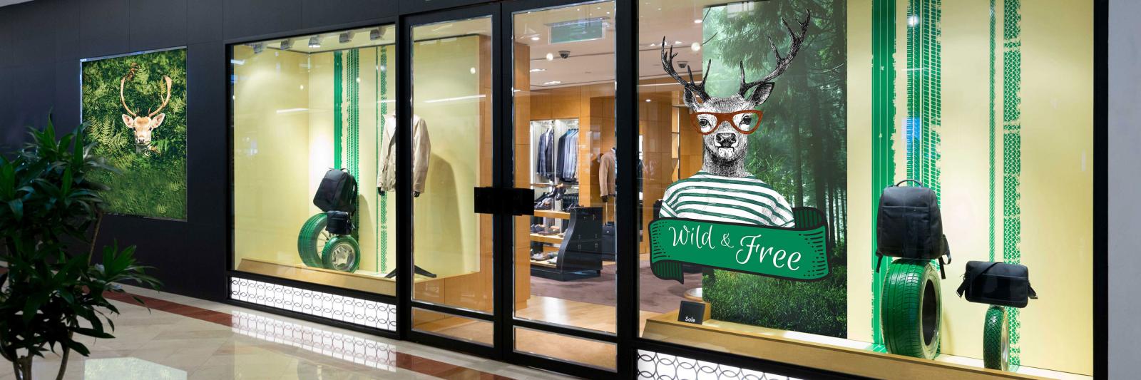Druckmedien selbstklebend für Werbeschilder - Schaufenster Boutique mit grüner Werbung und Hirsch mit Brille und T-Shirt